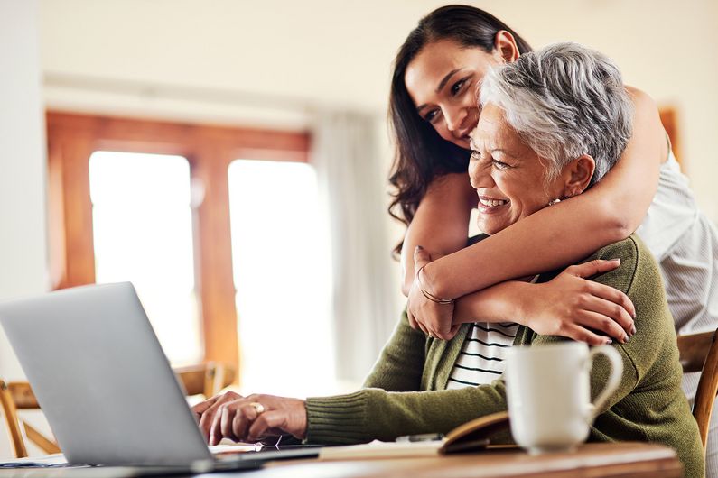 Frau umarmt ihre Mutter, die vor einem Laptop sitzt